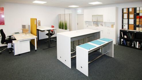 Büroeinrichtung mit weißem Holz Zwei weiße Stehtische vor weißen Schreibtischen auf grauem Teppich